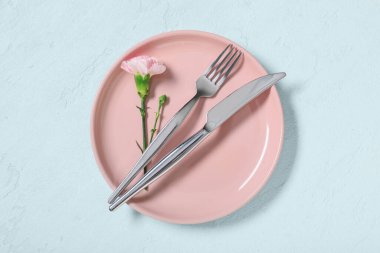 Gümüş çatal bıçak takımı ve açık mavi arka planda karanfil çiçeği olan güzel bir masa.