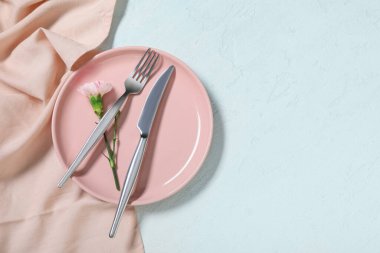 Gümüş çatal bıçak takımı ve açık mavi arka planda karanfil çiçeği olan güzel bir masa.