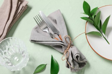 Gümüş çatal bıçak takımı ve yeşil arka planda taze yapraklarla güzel bir masa.