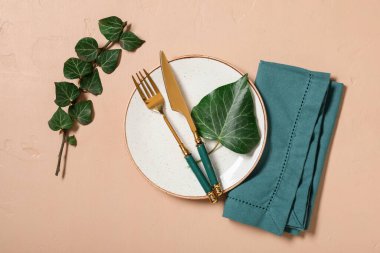 Altın çatal bıçak seti ve bej arka planda ağaç dalı olan güzel bir masa.