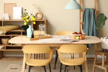 Yemek masasında limon ağacı dalları, bardaklar ve meyve sepeti olan bir vazo.