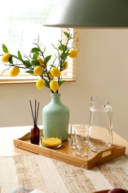 Limon ağacı dallı vazo, sürahi ve bardaklar yemek masasında.