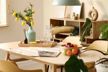 Yemek masasında limon ağacı dalları, bardaklar ve meyve sepeti olan bir vazo.