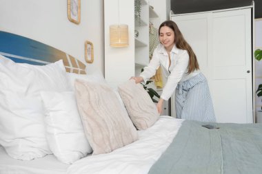 Yatak odasında sörf tahtasıyla yastığı ayarlayan genç bir kadın.