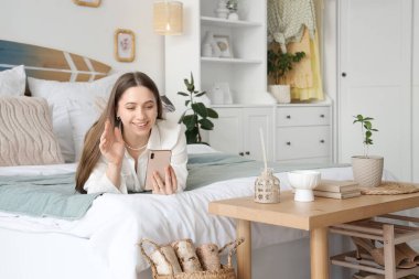 Yatakta cep telefonu, yatak odasında sörf tahtası kullanan genç bir kadın.