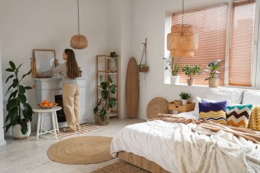 Genç bir kadın şömineye boş bir çerçeve ve yatak odasında sörf tahtası koyuyor.