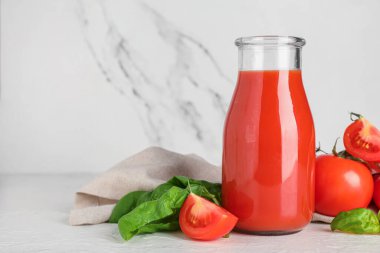 Beyaz arka planda fesleğen ve sebzeli bir şişe taze domates suyu.