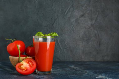 Koyu arkaplanda fesleğen ve sebzeli bir bardak taze domates suyu.