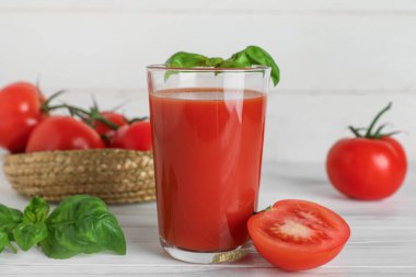 Beyaz ahşap arka planda fesleğen ve sebzeli bir bardak taze domates suyu.