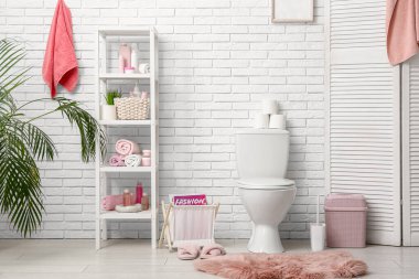 Seramik klozeti, raf ünitesi ve kürk halısı olan şık bir tuvalet.