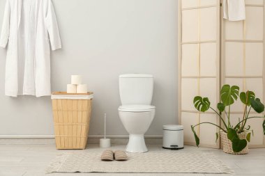Seramik klozet, çöp kutusu ve sepeti olan şık bir tuvalet.