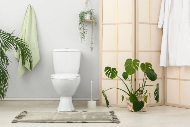 İçinde seramik klozet, ev bitkileri ve katlanan ekran olan şık tuvaletler.