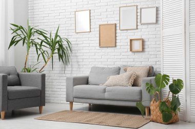 Gri kanepesi, çerçeveleri, çiçekleri ve katlanır perdesi olan şık bir oturma odası.