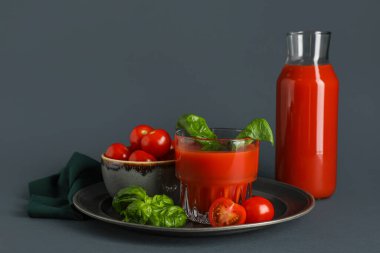 Koyu arkaplanda fesleğen ve bir şişe taze domates suyu.