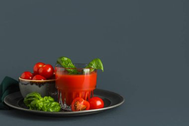 Koyu arkaplanda fesleğen ve sebzeli bir bardak taze domates suyu.