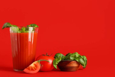 Kırmızı arka planda fesleğenli bir bardak taze domates suyu