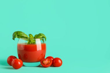 Turkuaz arka planda fesleğenli ve sebzeli bir bardak taze domates suyu.