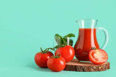 Turkuaz arka planda fesleğen ve sebzeli bir sürahi taze domates suyu.