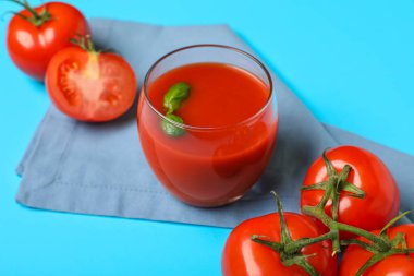 Mavi arka planda fesleğen ve sebzeli bir bardak taze domates suyu.