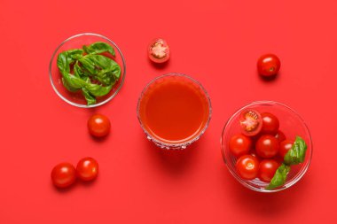 Kırmızı arka planda fesleğen ve sebzeli bir bardak taze domates suyu.