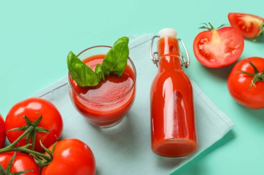 Turkuaz arka planda fesleğenli bir şişe ve bir bardak taze domates suyu.