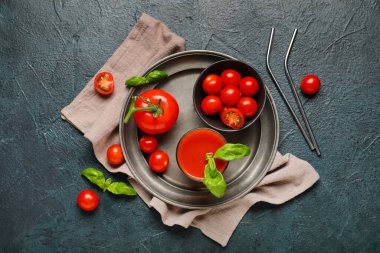 Koyu arkaplanda fesleğen ve sebzeli bir bardak taze domates suyu.