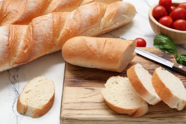 Beyaz arka planda kesilmiş taze baget, fesleğen ve kiraz domatesli ahşap tahta, yakın plan.