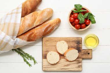 Beyaz ahşap arka planda taze baget, biberiye ve kiraz domatesli tahta dilimleri.