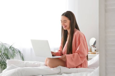 Yatak odasında dizüstü bilgisayar kullanan mutlu genç bir kadının sabahı.
