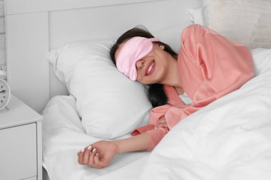 Sabah mutlu genç bir kadın uyku maskesiyle yatak odasında yatıyor.