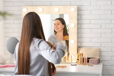 Genç bir kadının yatak odasındaki aynanın yanında saç taradığı bir sabah.