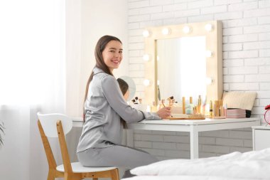 Mutlu genç bir kadının makyaj yaptığı bir sabah. Yatak odasındaki aynanın yanında.