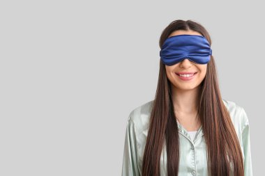 Açık arkaplanda uyku maskesi olan pijamalı genç bir kadın.