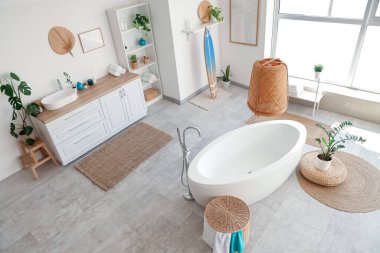 Küveti, çiçekleri ve sörf tahtasıyla aydınlık banyonun içi.