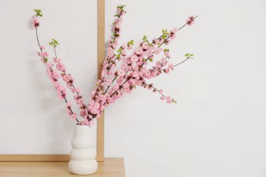 Işık duvarının yanındaki rafta pembe çiçekli bir vazo.