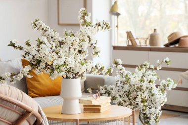 Oturma odasında çiçek açan dalları, güneş gözlükleri ve kitapları olan bir vazo.