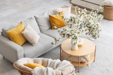 Kanepesi, koltuğu ve vazoda çiçekli dallarıyla aydınlık oturma odasının içinde.