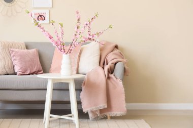 Oturma odasının içinde, kanepede ve vazoda pembe çiçekli dallarla.