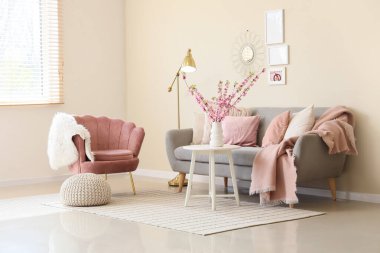 Oturma odasının içinde kanepe, pembe koltuk ve vazoda çiçek açan dallar var.