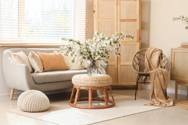 Oturma odasının içinde kanepe, katlanan perde ve vazoda çiçek açan dallar.