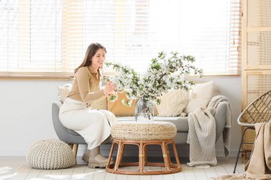 Oturma odasındaki dallarla kanepede oturan genç bir kadın.