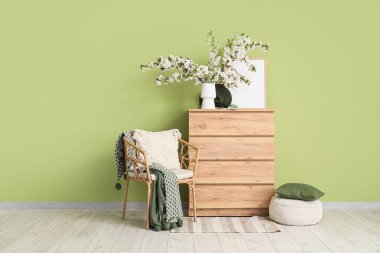 Oturma odasının içinde koltuk, tuvalet ve vazoda çiçek açan dallar var.