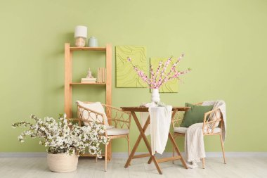 Oturma odasının içinde koltuklar, masa ve çiçek açan dallar var.