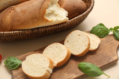 Tahta tahta ve hasır kâse. Taze baget ekmek ve bej arka planda fesleğen. Yakın plan.