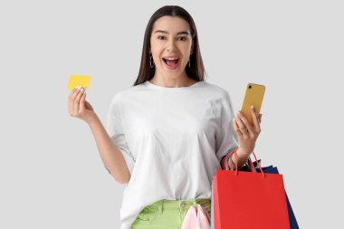 Cep telefonu ve kredi kartı ile beyaz arka planda online alışveriş yapan mutlu genç bir kadın.