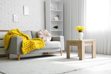 İçinde kanepe, raf ünitesi ve vazoda narsisleri olan oturma odası.