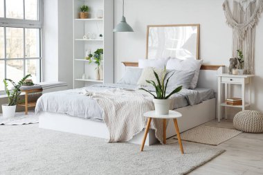 Konforlu yataklı, komodinli, çiçekli ve raflı bir yatak odası.