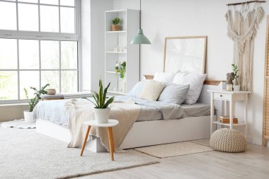 Konforlu yataklı, komodinli, çiçekli ve raflı bir yatak odası.