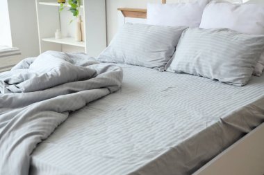 Yatak odasında yumuşak yastıkları ve buruşuk gri battaniyesi olan rahat bir yatak.