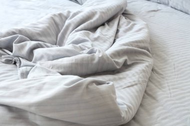 Yatak odasında buruşuk gri battaniyeli rahat yatak, yakın plan.